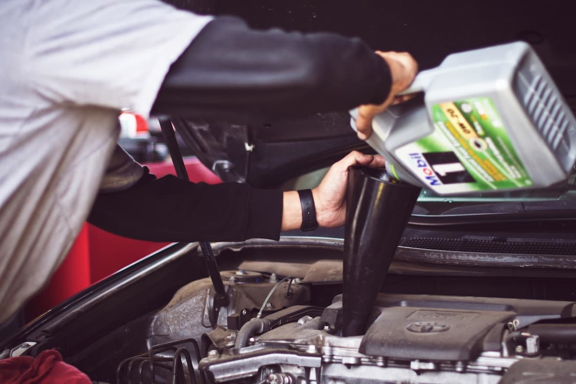 Person pouring engine oil into car engine using blue funnel
